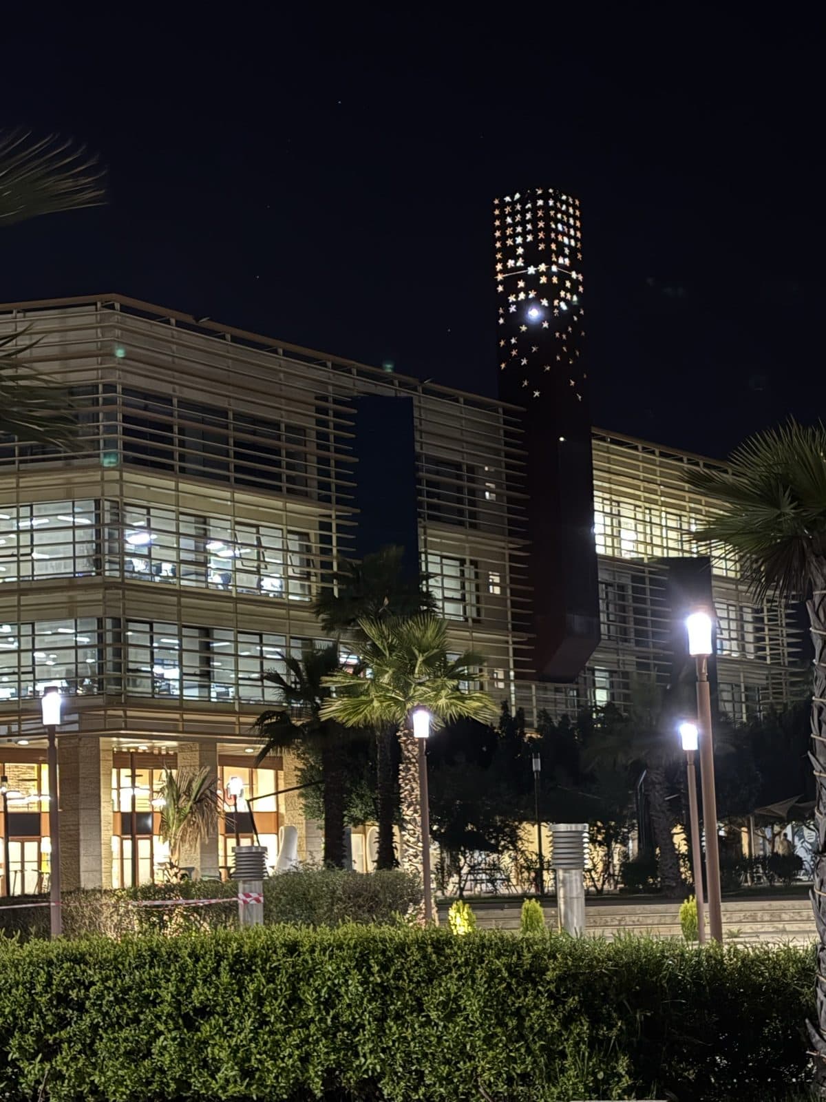 1337 Khouribga at night: lit classrooms behind the louvres, the rust-red tower glowing through its star-shaped perforations