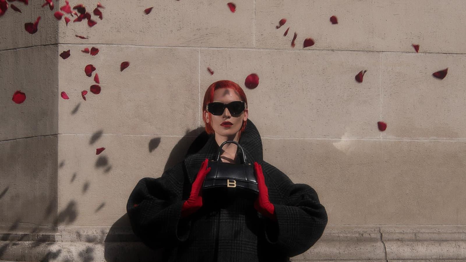 BeigePill campaign photograph: a woman in a black coat and red gloves holding a bag under the Avenue des Champs-Élysées sign, rose petals falling